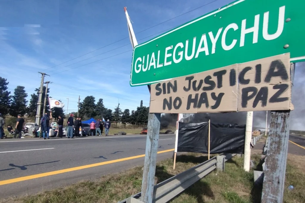 alt="Cartel manuscrito "Sin justicia no hay paz" colgado bajo el letrero de Gualeguaychú durante la protesta en la Autovía 14"