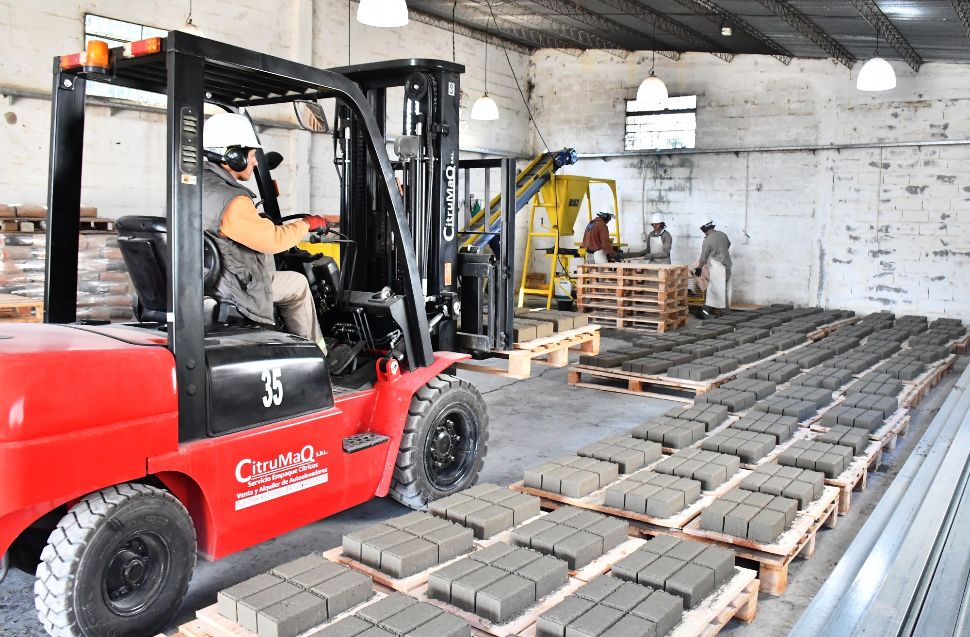 alt="Un montacargas rojo traslada pallets de bloques de cemento secados en la planta municipal de adoquines de Concordia"