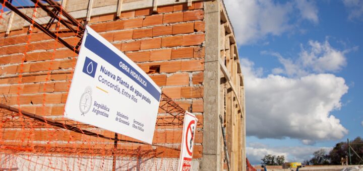 alt="Cartel de la obra de agua potable de Concordia frente al edificio de la nueva planta potabilizadora en construcción"