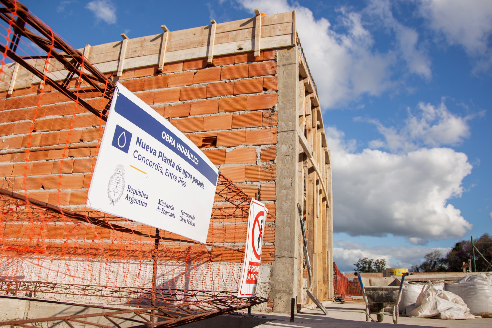 alt="Cartel de la obra de agua potable de Concordia frente al edificio de la nueva planta potabilizadora en construcción"