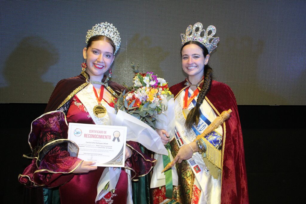 alt="La Reina Provincial del Inmigrante 2026 y la reina saliente Jazmín Busto Famularo comparten escenario durante la coronación"