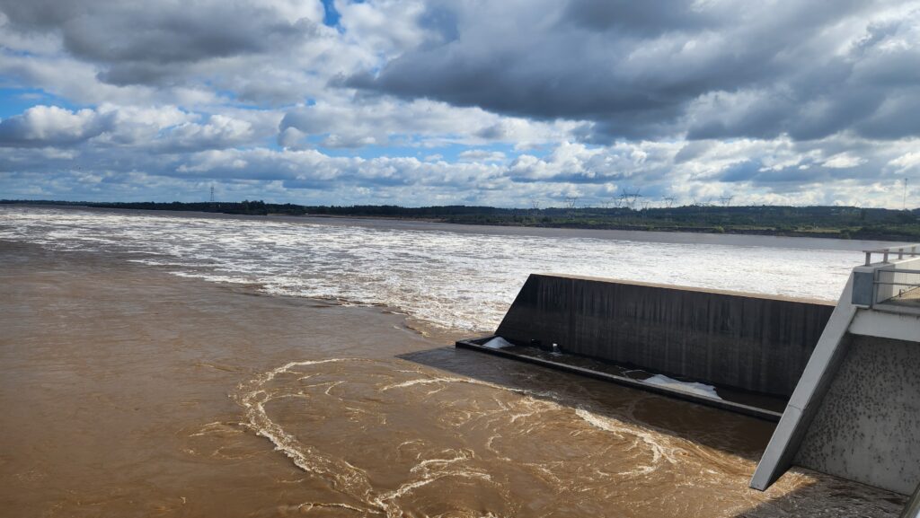 alt="Vertedero abierto de la represa de Salto Grande con agua marrón y espuma, en la crecida del río Uruguay en Concordia"
