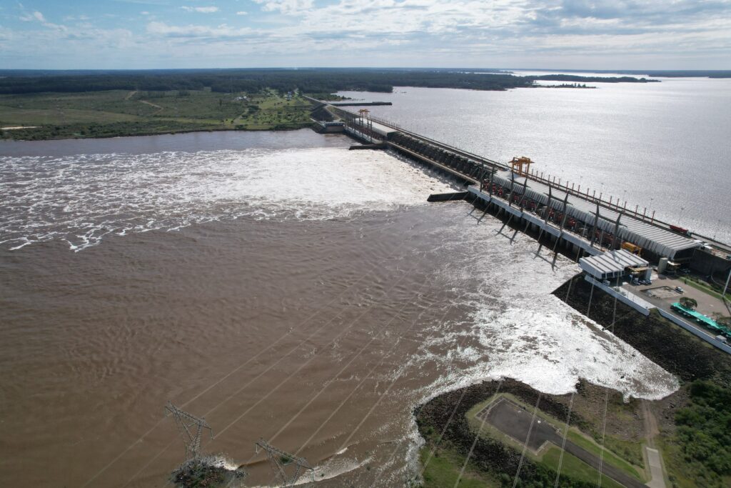 alt="Vista aérea de la represa de Salto Grande con descarga de agua marrón, relacionada con la crecida del río Uruguay en Concordia"