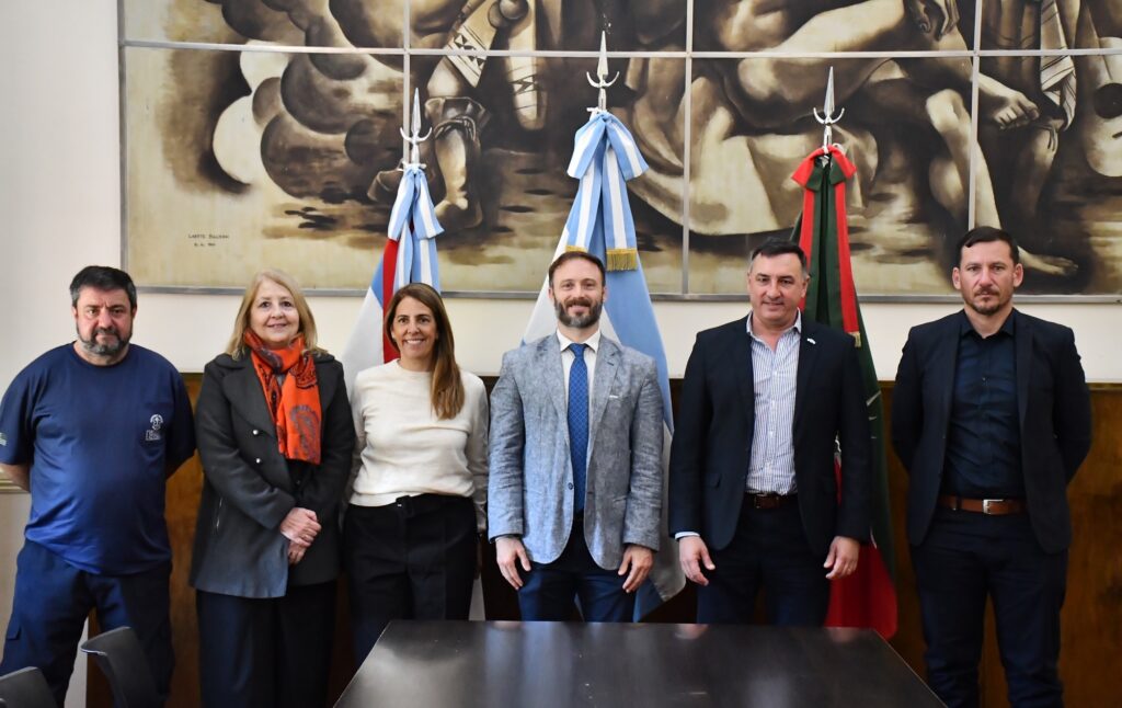 alt="Seis integrantes de las delegaciones de Concordia y Salto frente a las banderas, tras la reunión por la crecida del río Uruguay en Concordia"
