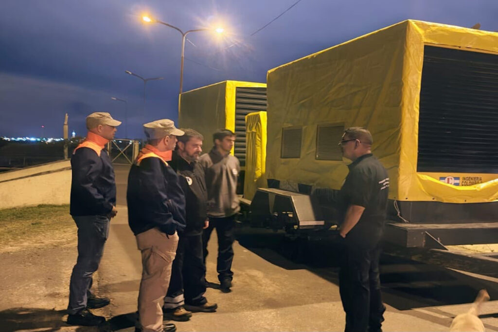 alt="Dos grupos electrógenos cubiertos con lonas amarillas, de noche, y cinco personas conversando junto a ellos, en una tarea de prevención ante El Niño en Entre Ríos"