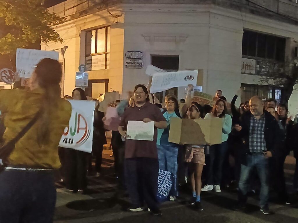 alt="•	Participantes con cartel de AGMER en la movilización nocturna por la reforma curricular de Jóvenes y Adultos"