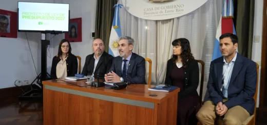 Ministro y funcionarios presentan el presupuesto provincial 2027 en un salón con las banderas de Entre Ríos y de Argentina.