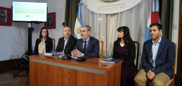 Ministro y funcionarios presentan el presupuesto provincial 2027 en un salón con las banderas de Entre Ríos y de Argentina.