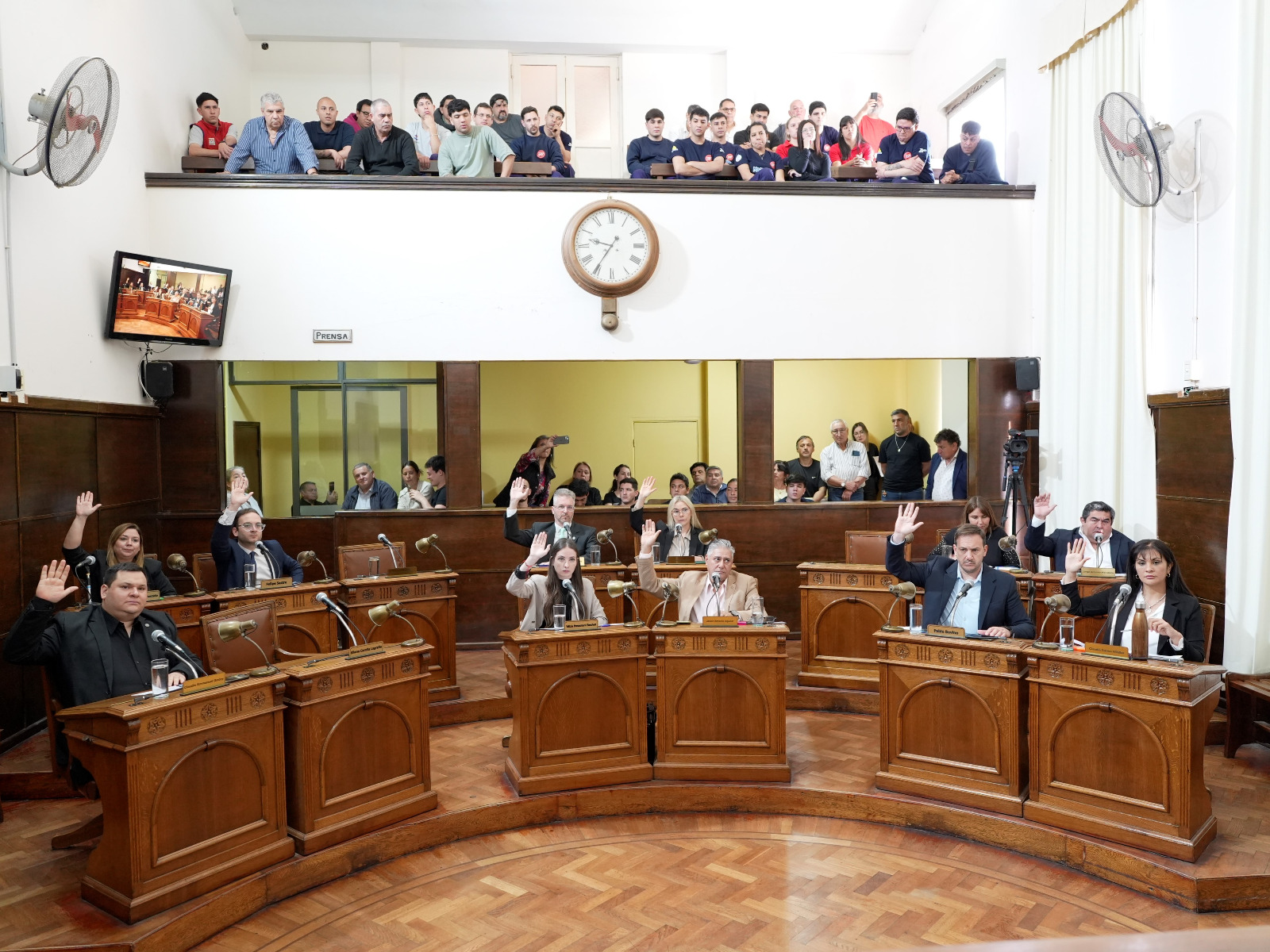 alt="Concejales de Concordia con la mano en alto durante la votación de la Ley de Grandes Superficies en Concordia, con público en la galería del recinto"